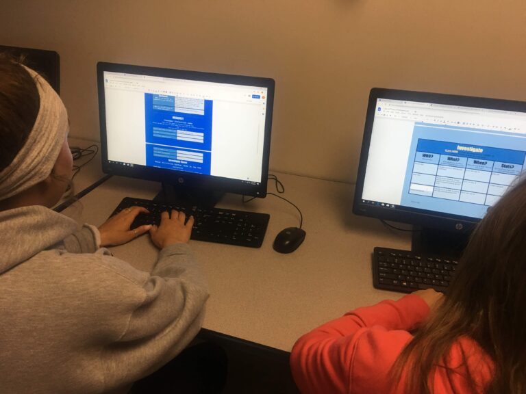 Two people sitting at a desk with computers.