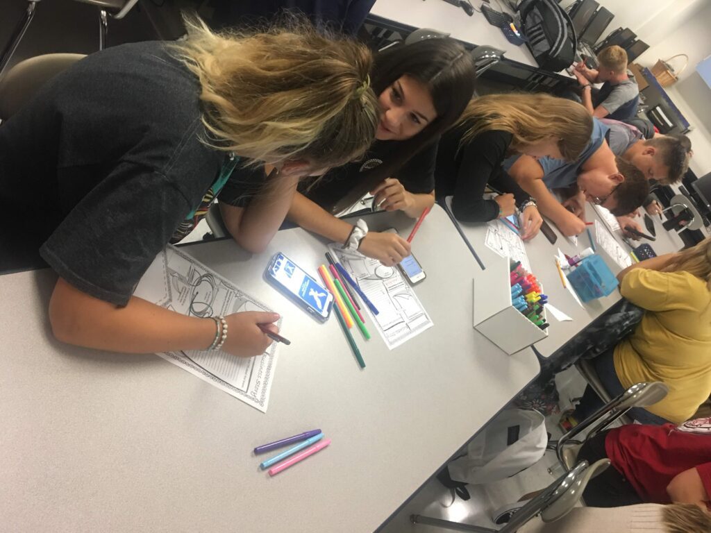 A group of people sitting at a table with pens and pencils.