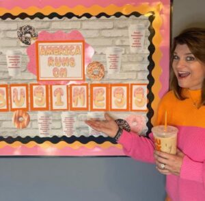 A woman holding a drink in front of a bulletin board.